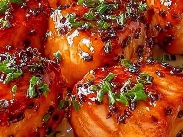Close-up of golden seared salmon bites drizzled with creamy orange bang bang sauce on a white plate.