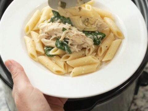 Creamy mozzarella spinach artichoke chicken in a slow cooker, with melted cheese and wilted greens.