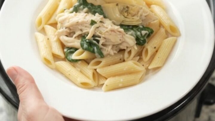 Creamy mozzarella spinach artichoke chicken in a slow cooker, with melted cheese and wilted greens.