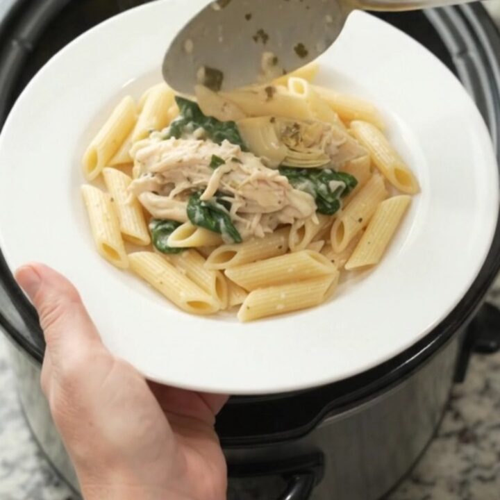 Creamy mozzarella spinach artichoke chicken in a slow cooker, with melted cheese and wilted greens.