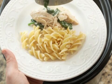 A creamy slow cooker chicken with spinach and artichokes, served over buttered egg noodles