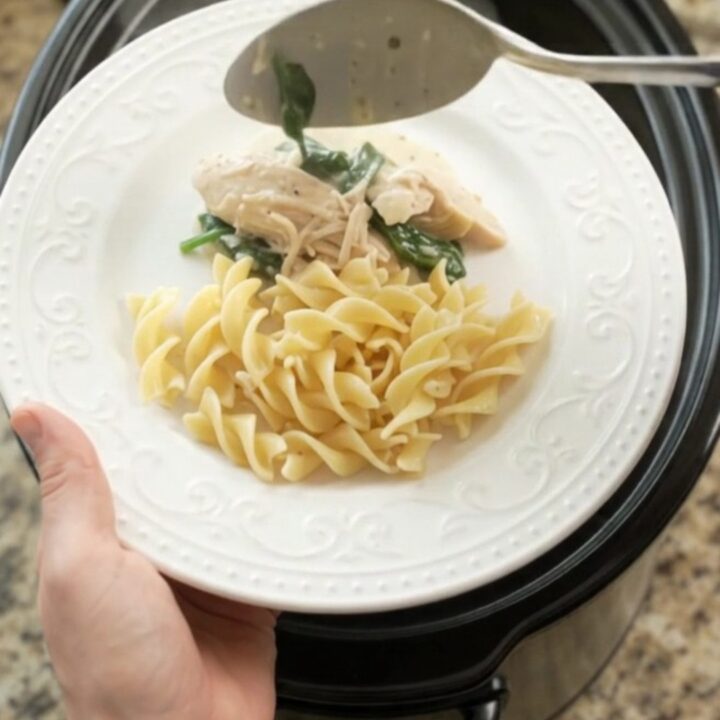 A creamy slow cooker chicken with spinach and artichokes, served over buttered egg noodles