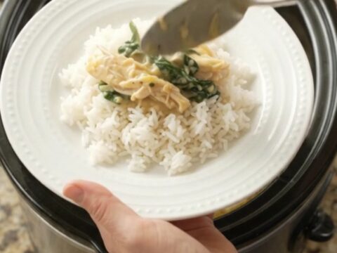 Creamy cheddar spinach artichoke chicken in a slow cooker, topped with melted cheese and fresh herbs.