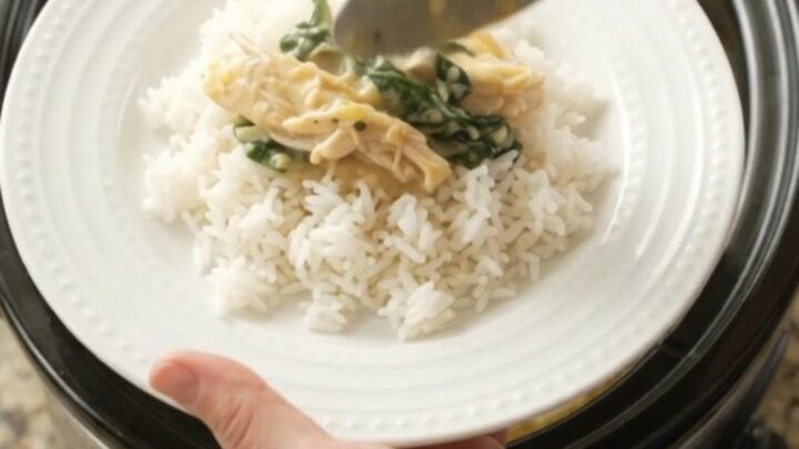 Creamy cheddar spinach artichoke chicken in a slow cooker, topped with melted cheese and fresh herbs.