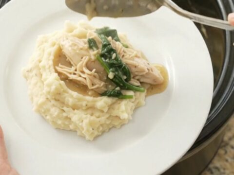 A slow cooker filled with creamy Swiss spinach artichoke chicken, with a spoon lifting a steaming bite.
