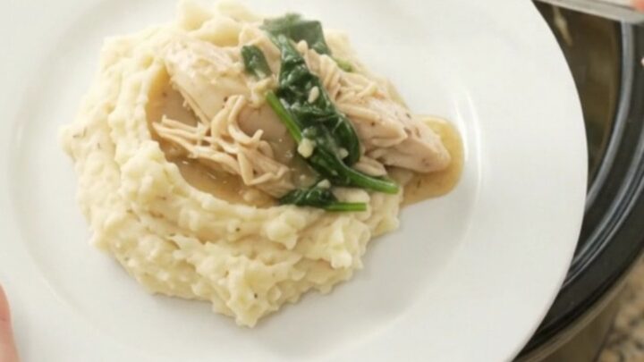 A slow cooker filled with creamy Swiss spinach artichoke chicken, with a spoon lifting a steaming bite.