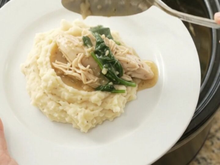 A slow cooker filled with creamy Swiss spinach artichoke chicken, with a spoon lifting a steaming bite.