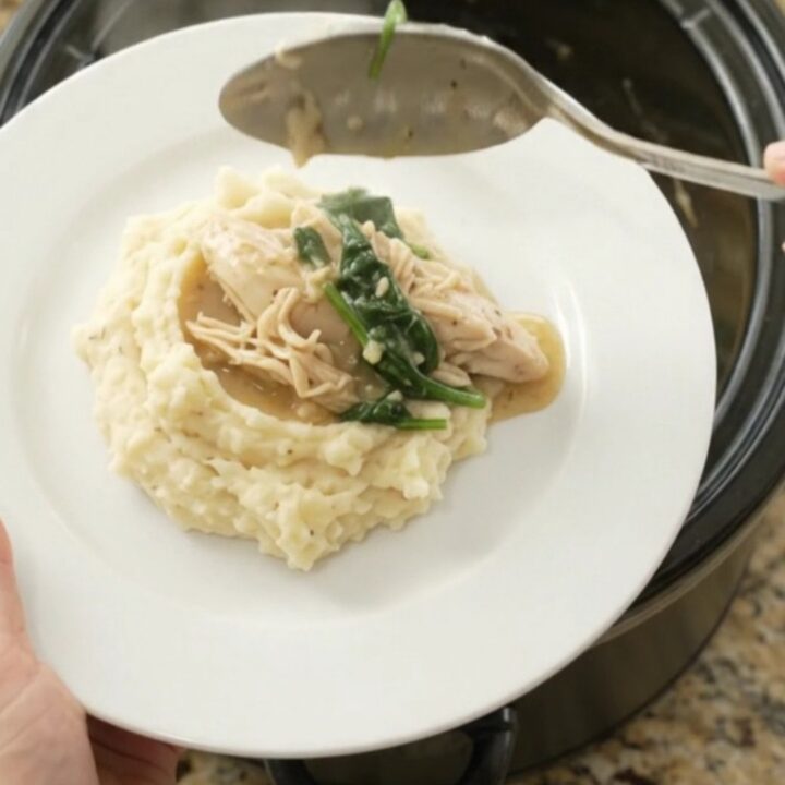 A slow cooker filled with creamy Swiss spinach artichoke chicken, with a spoon lifting a steaming bite.
