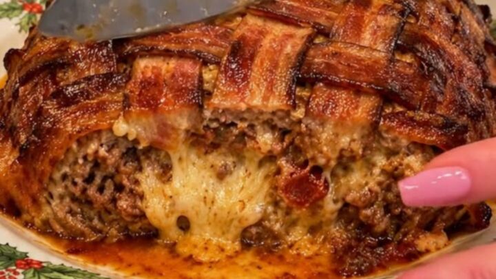 A crispy, golden-brown bacon-wrapped beef roast sitting on a festive white platter garnished with green holly leaves.