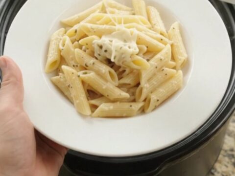 Creamy mozzarella sweet corn chicken in a slow cooker with a spoon lifting a cheesy scoop