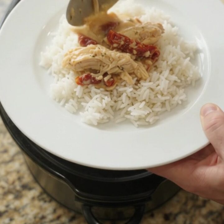 Creamy cheddar sun-dried tomato chicken in a slow cooker, bubbling with melted cheese and tomato ribbons.