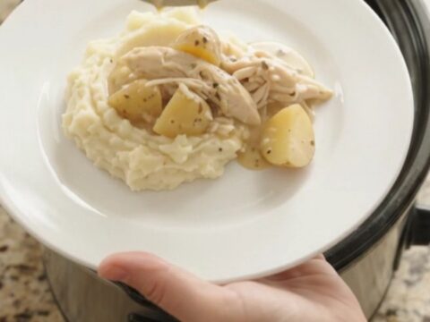 Creamy Swiss baby potato chicken in a slow cooker, topped with melted cheese and steam rising.