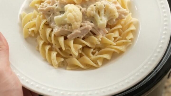 Creamy Parmesan cauliflower chicken in a slow cooker, with a spoon lifting a bite