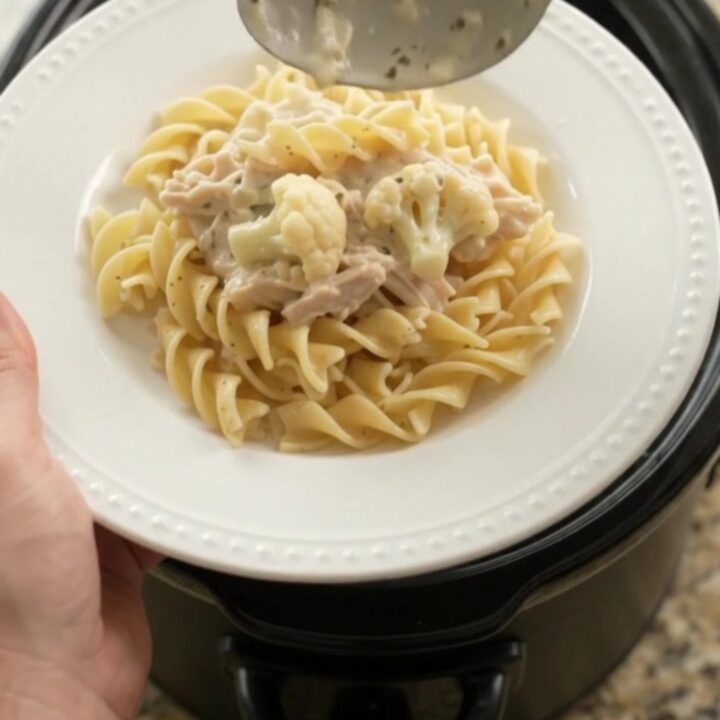 Creamy Parmesan cauliflower chicken in a slow cooker, with a spoon lifting a bite