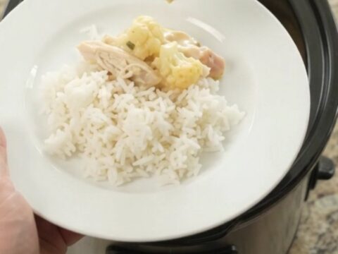 Creamy cheddar cauliflower chicken in a slow cooker, topped with melted cheese and herbs.