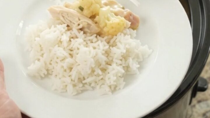 Creamy cheddar cauliflower chicken in a slow cooker, topped with melted cheese and herbs.