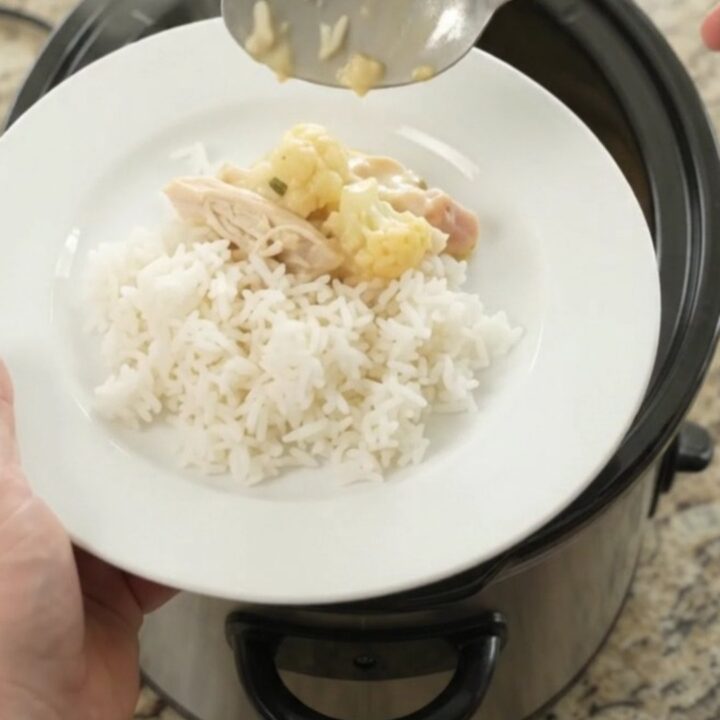 Creamy cheddar cauliflower chicken in a slow cooker, topped with melted cheese and herbs.