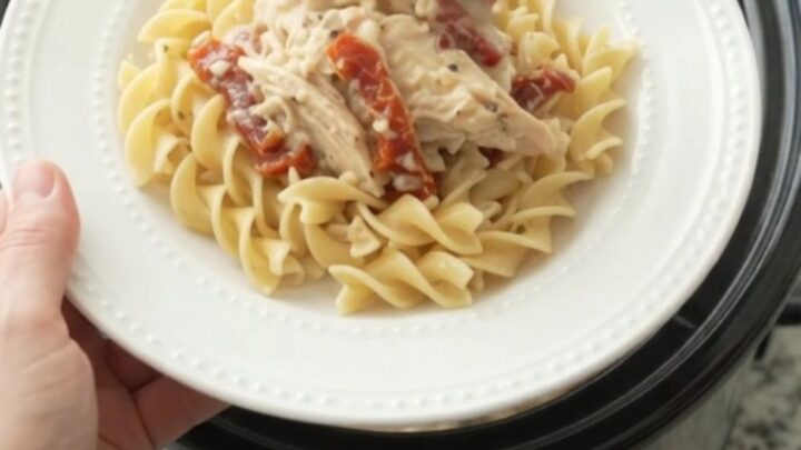 Slow cooker creamy Parmesan sun-dried tomato chicken in a black Crockpot, with steam rising.