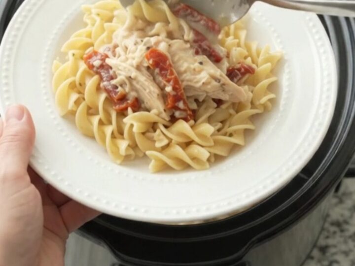 Slow cooker creamy Parmesan sun-dried tomato chicken in a black Crockpot, with steam rising.