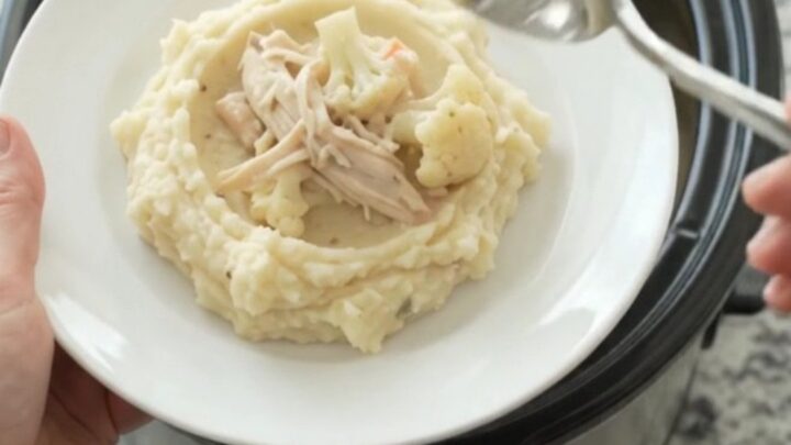 A slow cooker filled with creamy Swiss cauliflower chicken, with melted cheese and tender chicken pieces.