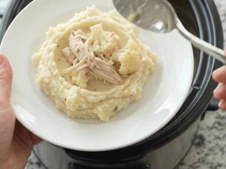 A slow cooker filled with creamy Swiss cauliflower chicken, with melted cheese and tender chicken pieces.