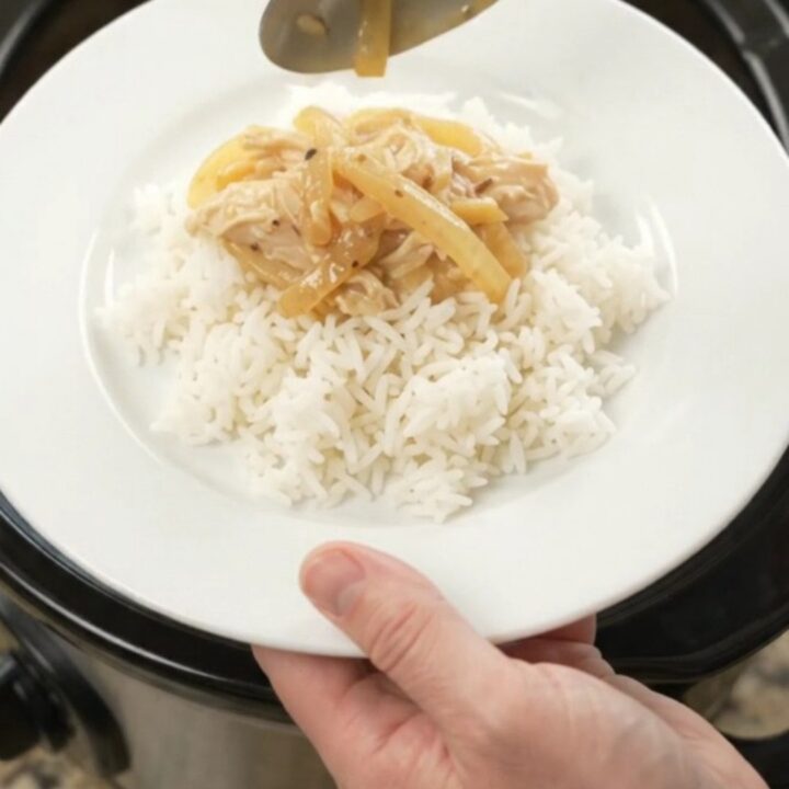 Creamy cheddar French onion chicken in a slow cooker, topped with melted cheese and caramelized onions