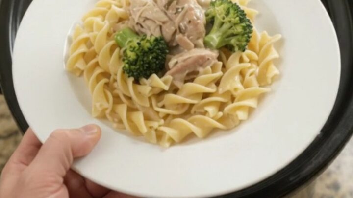 Creamy slow cooker chicken and broccoli in a black crockpot, with a spoon lifting a saucy bite.