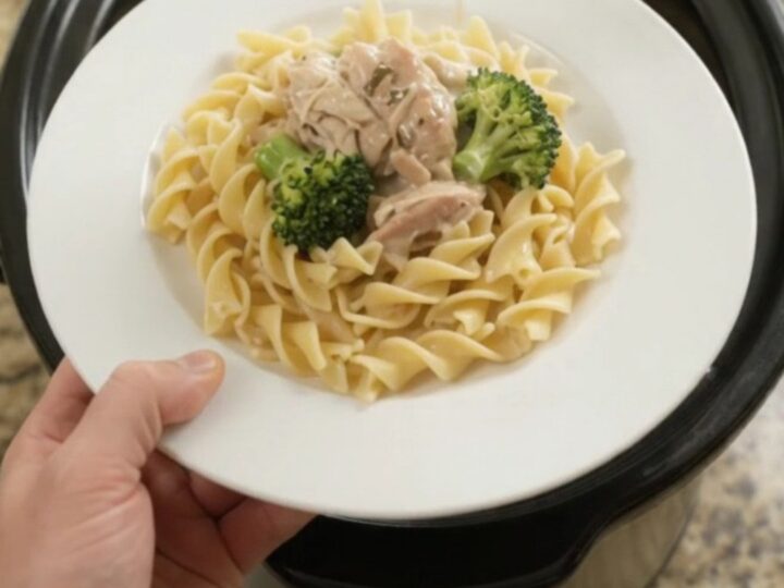 Creamy slow cooker chicken and broccoli in a black crockpot, with a spoon lifting a saucy bite.