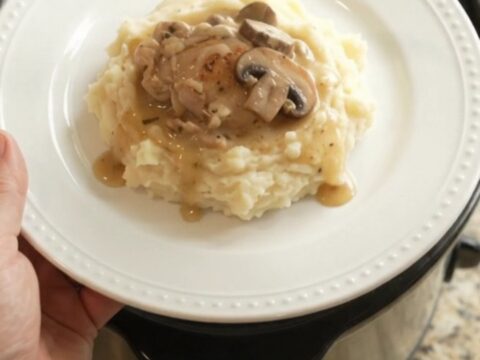 A slow cooker filled with creamy Swiss mushroom chicken thighs, with melted cheese and mushrooms visible in the sauce.
