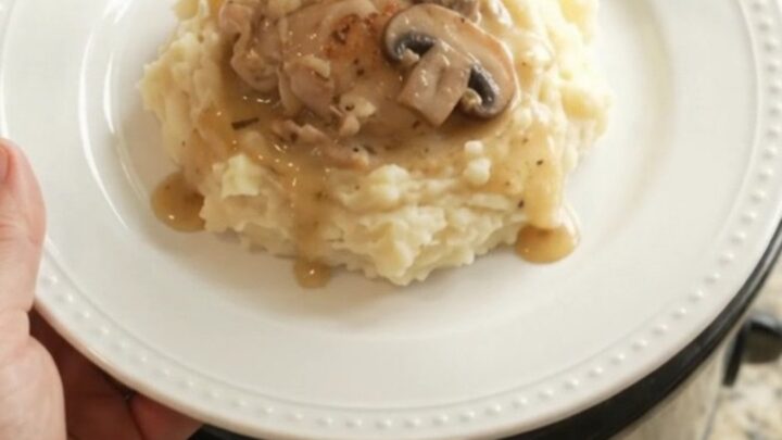 A slow cooker filled with creamy Swiss mushroom chicken thighs, with melted cheese and mushrooms visible in the sauce.