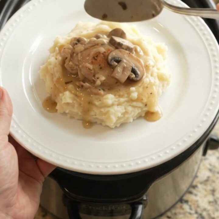 A slow cooker filled with creamy Swiss mushroom chicken thighs, with melted cheese and mushrooms visible in the sauce.