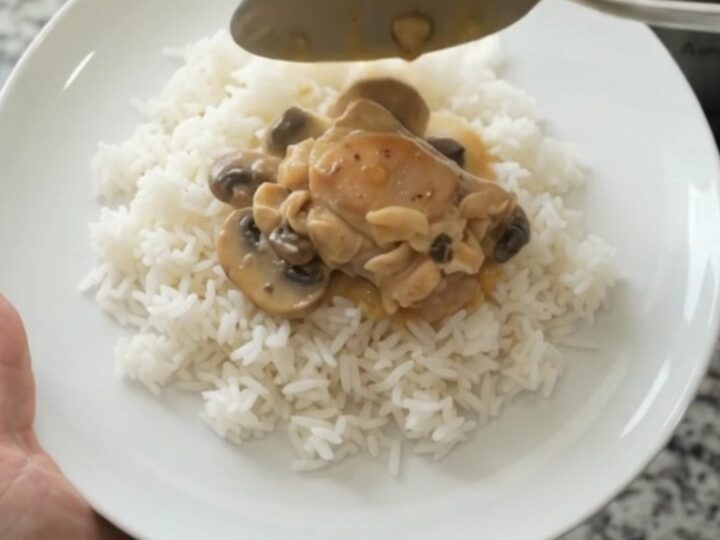 Slow cooker filled with creamy cheddar mushroom chicken thighs, topped with melted cheese and mushrooms.