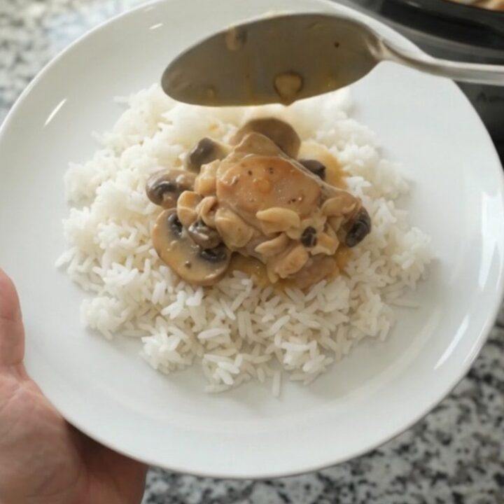 Slow cooker filled with creamy cheddar mushroom chicken thighs, topped with melted cheese and mushrooms.