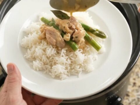 Creamy cheddar asparagus chicken thighs in a slow cooker, topped with melted cheese and butter.