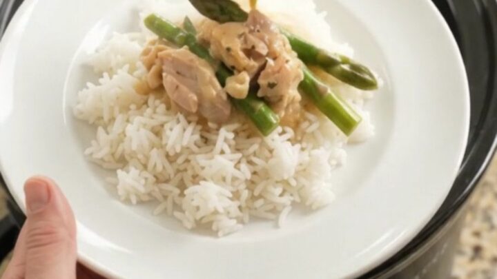 Creamy cheddar asparagus chicken thighs in a slow cooker, topped with melted cheese and butter.