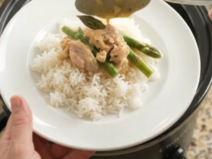 Creamy cheddar asparagus chicken thighs in a slow cooker, topped with melted cheese and butter.