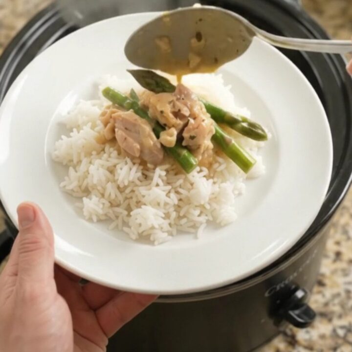 Creamy cheddar asparagus chicken thighs in a slow cooker, topped with melted cheese and butter.
