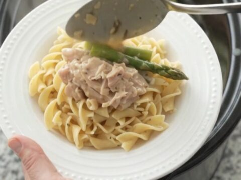 Creamy slow cooker chicken thighs with asparagus in a Parmesan sauce, served in a black crockpot