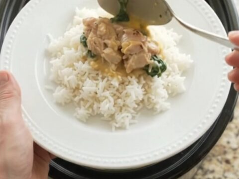 Creamy cheddar spinach artichoke chicken thighs in a slow cooker, with a spoon lifting a bite.
