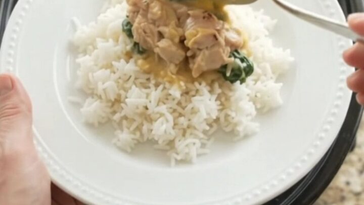 Creamy cheddar spinach artichoke chicken thighs in a slow cooker, with a spoon lifting a bite.