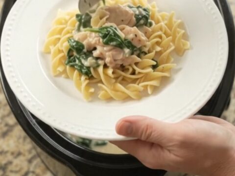 Slow cooker full of creamy spinach artichoke chicken with melted cheese and steam rising