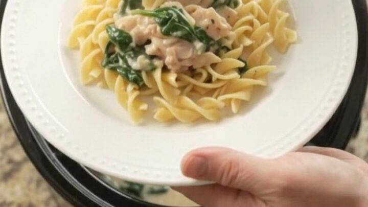Slow cooker full of creamy spinach artichoke chicken with melted cheese and steam rising