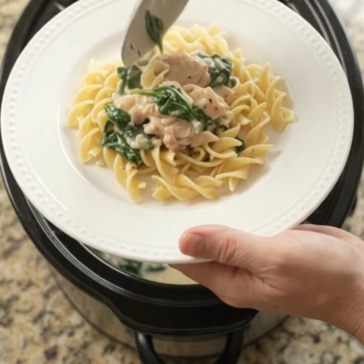 Slow cooker full of creamy spinach artichoke chicken with melted cheese and steam rising