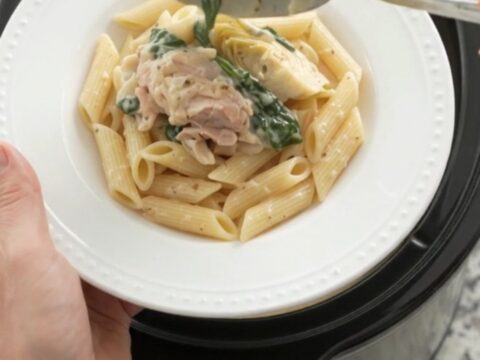 Slow cooker full of creamy spinach artichoke chicken with melted mozzarella