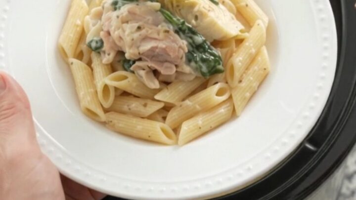 Slow cooker full of creamy spinach artichoke chicken with melted mozzarella