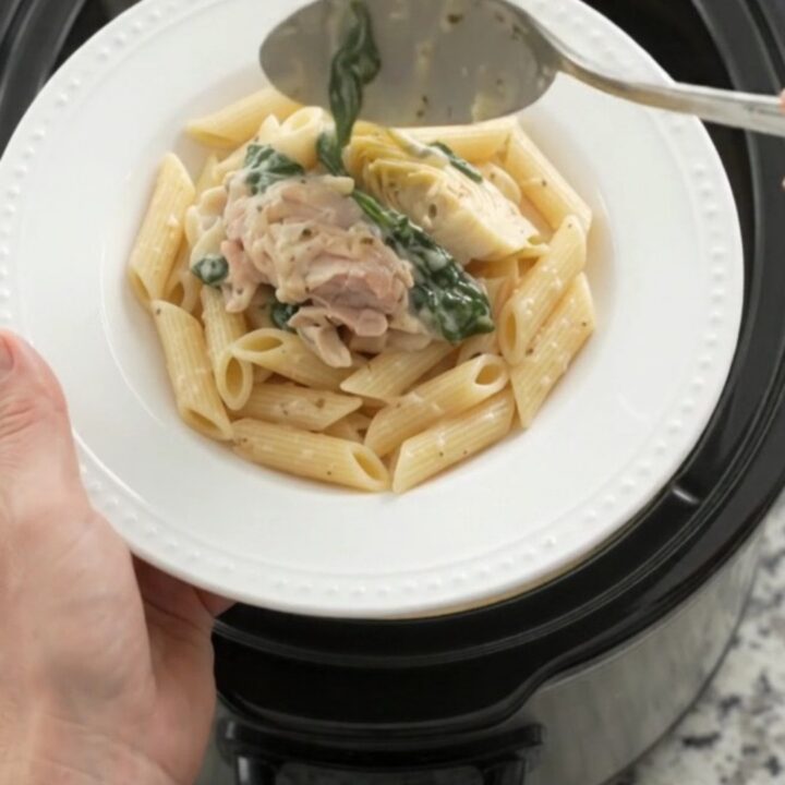 Slow cooker full of creamy spinach artichoke chicken with melted mozzarella