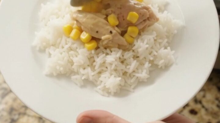 Creamy cheddar corn chicken thighs bubbling in a slow cooker, with melted cheese and golden corn visible.