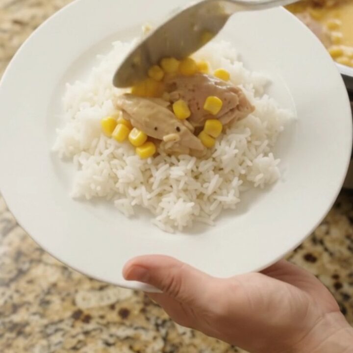 Creamy cheddar corn chicken thighs bubbling in a slow cooker, with melted cheese and golden corn visible.