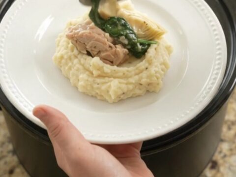 Creamy Swiss spinach artichoke chicken thighs in a slow cooker, topped with melted cheese and steam rising.