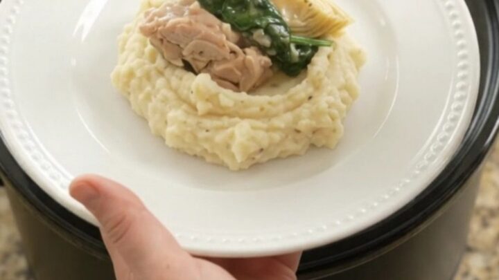 Creamy Swiss spinach artichoke chicken thighs in a slow cooker, topped with melted cheese and steam rising.